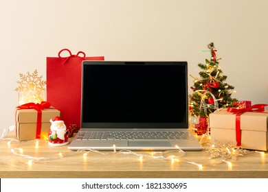 Laptop Mockup Among Gift Boxes, Paper Bag On Wooden Table With Garland Lights. Christmas Shopping Online Concept.