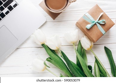 Laptop With Morning Coffee And Tulips And Stylish Gift Box On White Wooden Rustic Background. Flat Lay Freelance, Work Gadgets With Space For Text. Spring Holiday. Happy Women Day