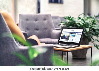 Laptop With News Website In Screen On Table In Business Office, Corporate Lounge Or Hotel Lobby. Company Wireless Wifi. Modern Cafe Or Workplace. Online Article In Computer. Woman On Chair Waiting. 