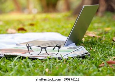 Laptop, Newspaper And Glasses On The Green Lawn. Select Focus