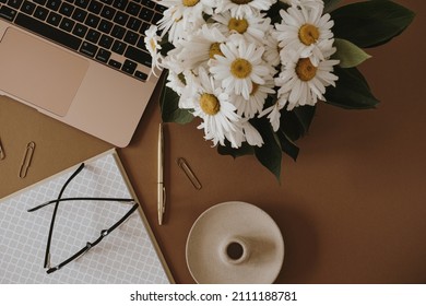 Laptop, Notebook, Chamomile Flowers Bouquet On Neutral Brown Background. Flat Lay, Top View Aesthetic Minimal Freelancer, Blogger Home Office Workspace