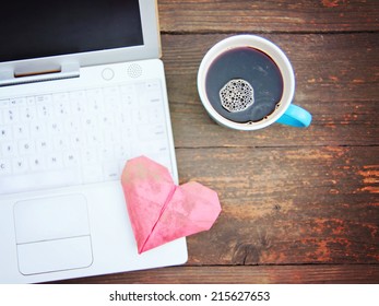 Laptop or notebook with cup of coffee and origami heart on old wooden table 