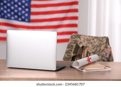 Laptop, notebooks and diploma on wooden table, chair with soldier uniform against flag of United States indoors. Military education - Powered by Shutterstock