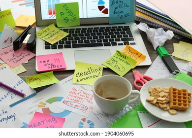 Laptop, notes and office stationery in mess on desk. Overwhelmed with work