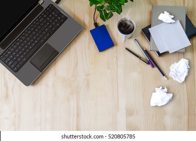 Laptop with office supplies, crumpled paper, green plant and hot black coffee with smoke on vintage grunge wooden desk background view from above, busy business concept