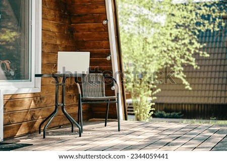 Laptop on the coffee table near whicker chair on terrace of log cabin. Concept of remote work and freelance.