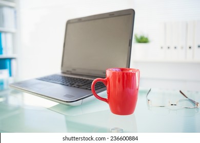 Laptop On Desk With Red Mug And Glasses In The Office