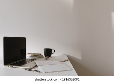 Laptop on table with coffee cup, paper sheet against white wall. Minimalist home office workspace. - Powered by Shutterstock