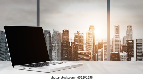 Laptop on table in office with panoramic sunset view of modern downtown skyscrapers at business district, blank screen - Powered by Shutterstock