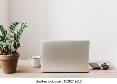 Laptop On Wooden Desktop With Phone, Notebook, Coffee Cup And Plant In Stylish Modern Room. Freelance Concept. Business Workspace In Home Or Office. Stylish Work Place. Working Online