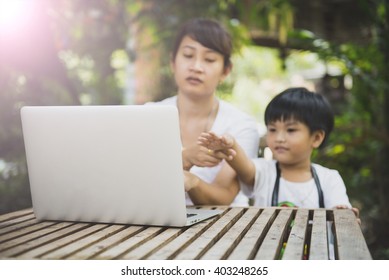 Laptop On The Wooden Table With Blur Of Son Asking Some Question To His Mom While His Mom Working.Vintage Style