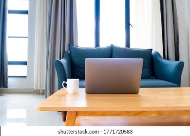 Laptop On Wooden Table With Sofa In Cozy Room, Set Up For Work From Home Workstation/online Learning.