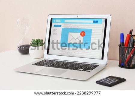 Laptop with opened e-mail box on table near light wall