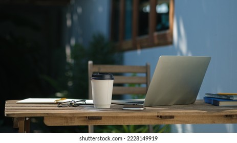 Laptop, paper cup of coffee, glasses and notebook on wooden table at outdoor. - Powered by Shutterstock