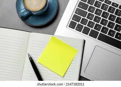 Laptop, planner, empty sticky note, pen and cup of coffee on grey table, flat lay. Space for design