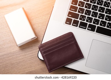 Laptop, Portable Power Bank, And Name Card Case On Wooden Table.