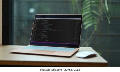 Laptop with programming code on screens and wireless mouse wooden office desk at software development company
