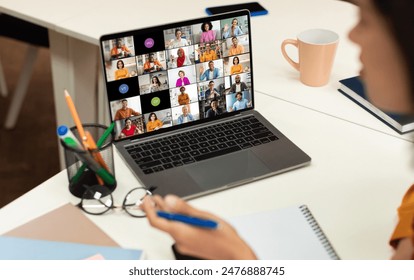 A laptop screen displays a video conference call with multiple participants of various backgrounds and ethnicities, all appearing in separate video squares.