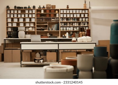 Laptop sitting on a table by shelves of pottery in a ceramics studio - Powered by Shutterstock