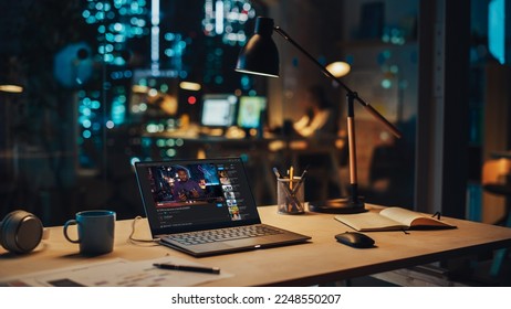 Laptop Standing on a Desk with a Video Streaming Platform Displayed on Screen. Table with Computer, Coffee Mug, Headphones and Notebook in Creative Office at Night. - Shutterstock ID 2248550207