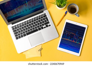 Laptop and tablet computer with stock data and cup of coffee on yellow background. Finance trading