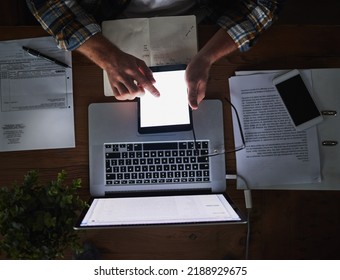 Laptop and tablet in the hands of a man working late at night in the office from above. Deadline and overtime at a desk with technology and paper work. Sending an email reading or typing a report - Shutterstock ID 2188929675