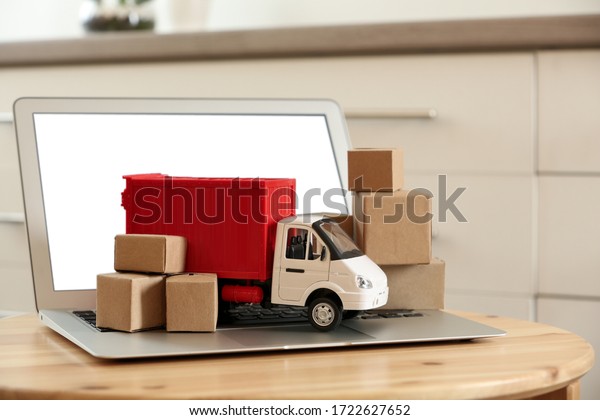 Laptop and truck model with boxes on table\
indoors. Courier service