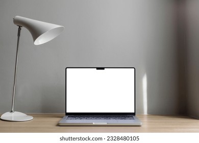 laptop with white screen on a wooden table. Gray background. White lamp on the table