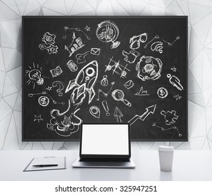 A laptop with white screen, a writing pad and a cap of coffee are on the white table. Business or educational icons are drawn on the black chalkboard. 3D rendering. - Powered by Shutterstock