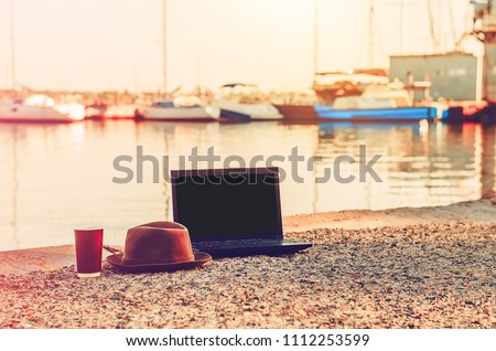 laptop for work and communication. wireless internet. freelancing. hot coffee. drink in the glass. dawn by the sea. yachts. hat