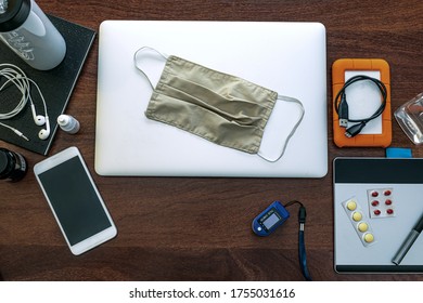 A Laptop To Work At Home, Agenda, HD, Cell Phone, Graphics Tablet, Headset, Surgical Mask, Pff2 Mask And Pulse Oximeter. On Top Of A Wooden Office Table. Top View. Home Office Concept.