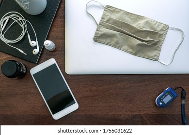 A Laptop To Work At Home, Agenda, HD, Cell Phone, Graphics Tablet, Headset, Surgical Mask, Pff2 Mask And Pulse Oximeter. On Top Of A Wooden Office Table. Top View. Home Office Concept.