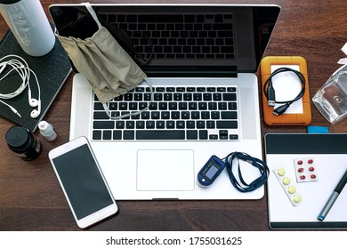 A Laptop To Work At Home, Agenda, HD, Cell Phone, Graphics Tablet, Headset, Surgical Mask, Pff2 Mask And Pulse Oximeter. On Top Of A Wooden Office Table. Top View. Home Office Concept.