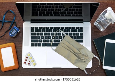 A Laptop To Work At Home, Agenda, HD, Cell Phone, Graphics Tablet, Headset, Surgical Mask, Pff2 Mask And Pulse Oximeter. On Top Of A Wooden Office Table. Top View. Home Office Concept.