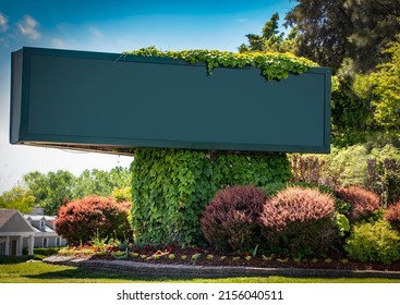 Large advertising sign -blank and copy space - on corner landscaped with vines and flowerbeds with trees and buildings in background