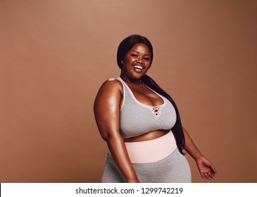 Large african woman looking happy on brown background. Plus size female in sports clothing looking at camera and laughing.
