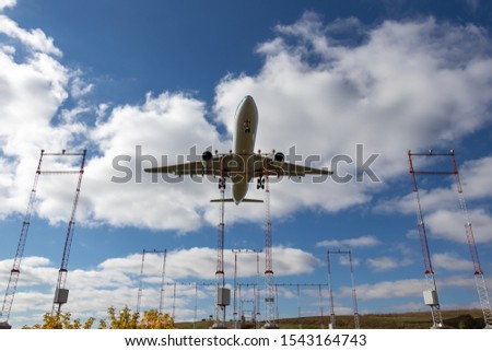 Large aircraft seen overhead landing over runway approach lights on a partly cloudy day.