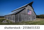 A large American flag adorns the side of an old wooden barn on a cloud-free day west of Atchison, Kansas.