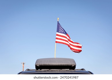 A large American Flag on top of a car against clear blue sky. American Flag waving on a roof of a car - Powered by Shutterstock