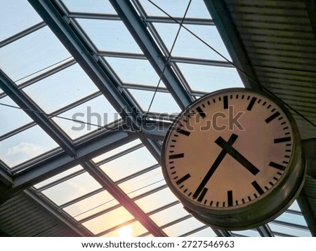 Large Analog Station Clock Under Glass Roof at Sunset. A classic railway station clock illuminated by warm sunset light that evokes travel and the passage of time.