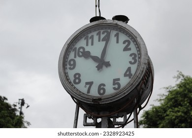 A large antique round clock in the city against a backdrop of white sky and green leaves of trees - Shutterstock ID 2328923425
