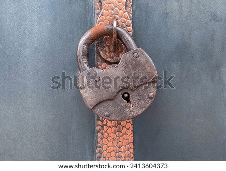 Large antique vintage padlocked barn mortise rusted metal lock on a gray painted background.