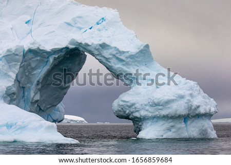 Large arch of ice as a gate through iceberg shimmers bluish close up