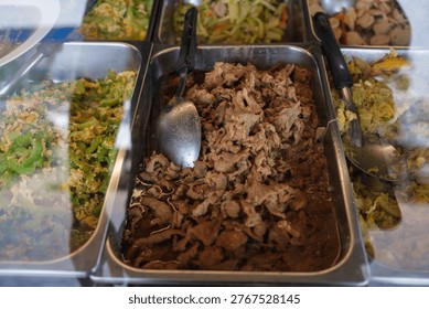 A large array of stainless steel trays filled with various colorful Thai curries and stir-fried dishes displayed for customers at a local street food market.