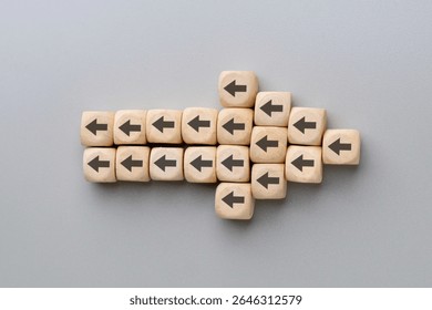 A large arrow formed by multiple wooden blocks with black arrows pointing in the opposite direction. Resistance to change, conflicting directions, stubbornness concept.