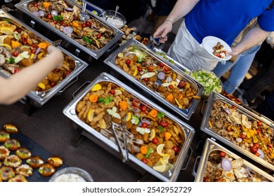 A large assortment of food is laid out on several tables, with guests serving themselves from the buffet. Colorful salads, grilled meats, and garnished platters decorate the space. - Powered by Shutterstock