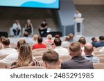 Large audience listens to speakers during a panel discussion at a tech conference. The room is filled with engaged attendees.