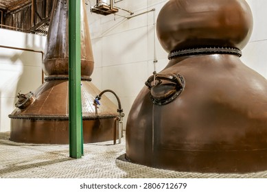 Large, authentic copper pot stills used for distilling high-quality whiskey, bourbon, or rum. Industrial interior view of a commercial distillery factory with equipment for alcohol production.