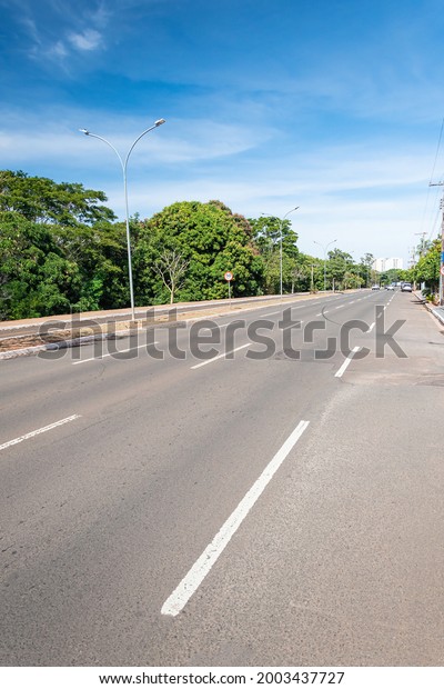Large avenue\
with a separated bike lane and green trees around. Nelly Martins\
avenue at Campo Grande MS,\
Brazil.
