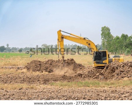 Large backhoe loader performing groundwork and soil excavation in an open field under a clear blue sky.